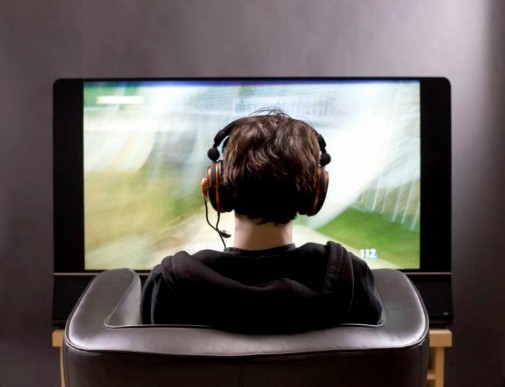 Teenage boy sits in front of TV playing video game